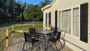 Eine Terrasse mit Tisch und Stühlen, ein Holzzaun und ein Haus mit großen Fenstern und einer Tür.