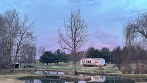 Ländliche Landschaft mit einem kleinen Haus, einem Teich und Bäumen.