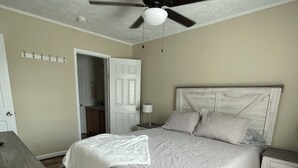 Ein Schlafzimmer mit Bett, Nachttisch, Deckenventilator, Tür und Kleiderständer.