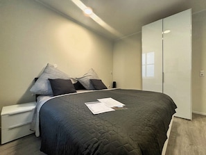 A bedroom with a bed, pillows, a nightstand, a wardrobe, and a bedside table.