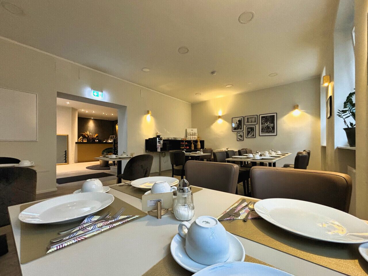 Un espace repas avec des tables dressées pour quatre personnes, agrémenté d’assiettes blanches, de couverts et d’une théière.