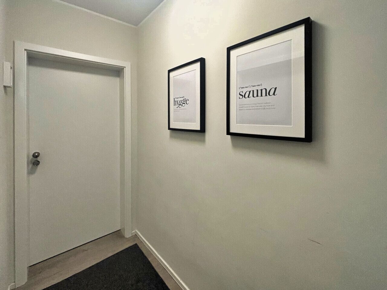 Un pasillo con dos letreros enmarcados en la pared, uno que dice “hygg” y el otro “sauna.”