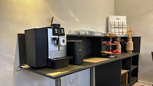 Une petite cuisine moderne équipée d’une machine à café, d’un petit réfrigérateur et d’un présentoir à fruits.