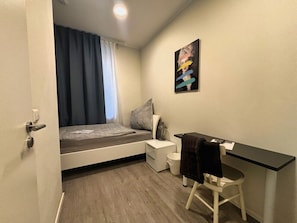 Une petite pièce comprenant un lit, une table de chevet, une chaise et un bureau.