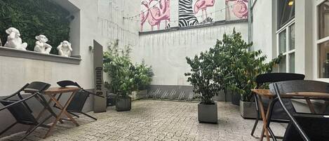Un espace extérieur aménagé avec des chaises et des tables, des plantes en pot et une fresque représentant des flamants roses et un zèbre sur le mur.