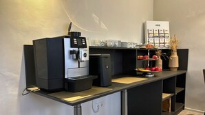 Una kitchenette moderna con una cafetera, un refrigerador pequeño y una exposición de frutas.