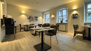 Un área de comedor moderna con varias mesas y sillas, iluminación empotrada en el techo y obras de arte en las paredes.