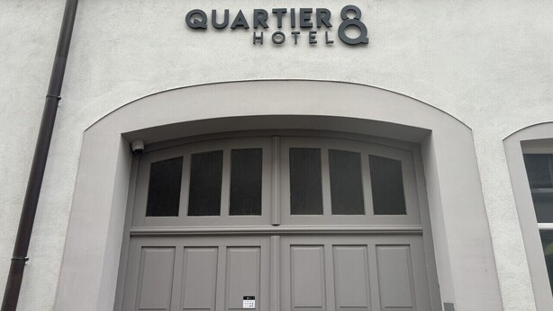 Exterior del Hotel Quartier, con una amplia entrada en arco y un cartel sobre las puertas.