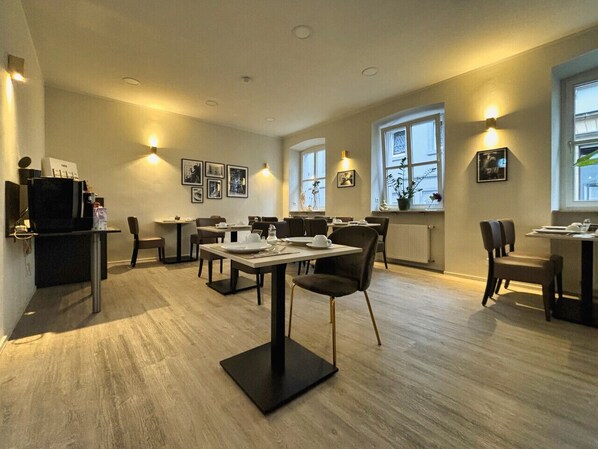 Un espace de restauration moderne, doté de plusieurs tables et chaises, d’appliques murales et de grandes fenêtres laissant entrer la lumière naturelle.