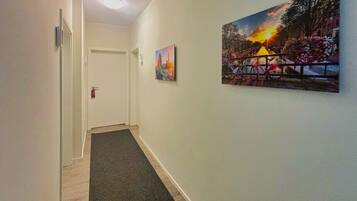 A hallway with a dark carpet, white walls, and two paintings depicting outdoor scenes.