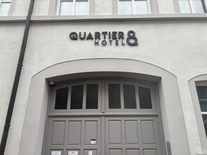 The exterior of the Quartier Hotel with a large arched entrance and a sign above the doors.