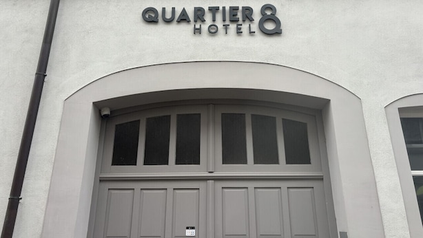 Exterior del Hotel Quartier, con una amplia entrada en arco y un cartel sobre las puertas.