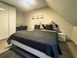 A bedroom with a bed, bedside tables, a wardrobe, and a desk with chairs. There are three framed pictures on the wall.