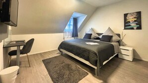Et moderne soveværelse med seng, skrivebord, stol og et billede på væggen.
