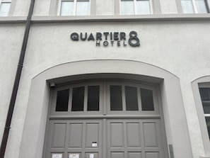 L’extérieur de l’hôtel Quartier présente une grande entrée en arc de cercle et une enseigne au-dessus des portes.