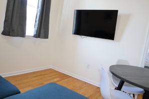 A room with a flat-screen TV mounted on the wall, a dining table with chairs, and a blue sofa.