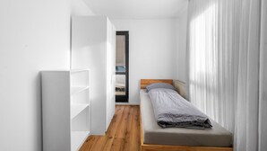 A small, modern bedroom with a single bed, a wardrobe, and a window with sheer curtains. - Havenu Oberkochen-Mitte - Doppelzimmer (Oberkochen)
