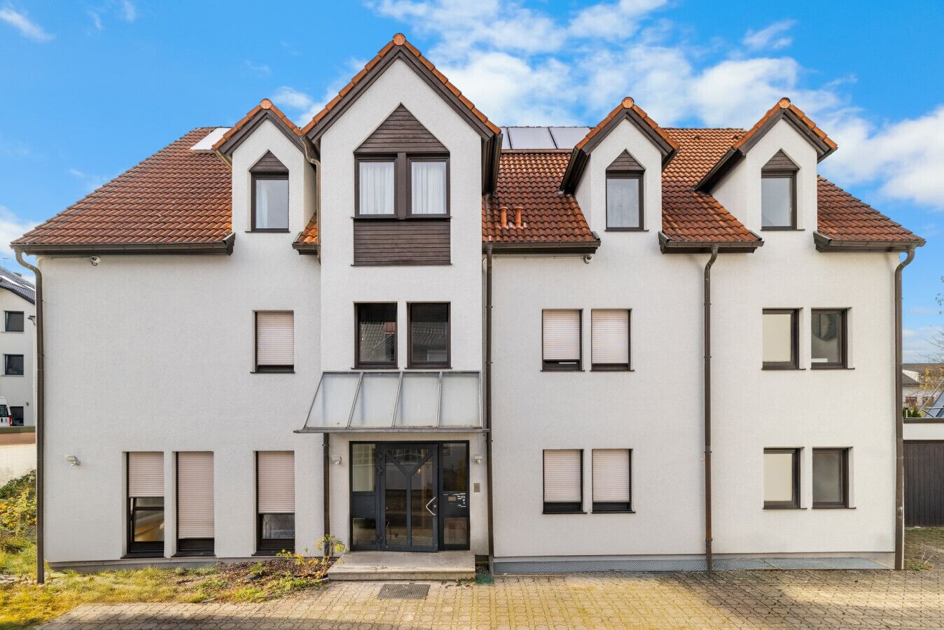 A multi-story residential building with a symmetrical facade, dormer windows, and a central entrance with a glass door.