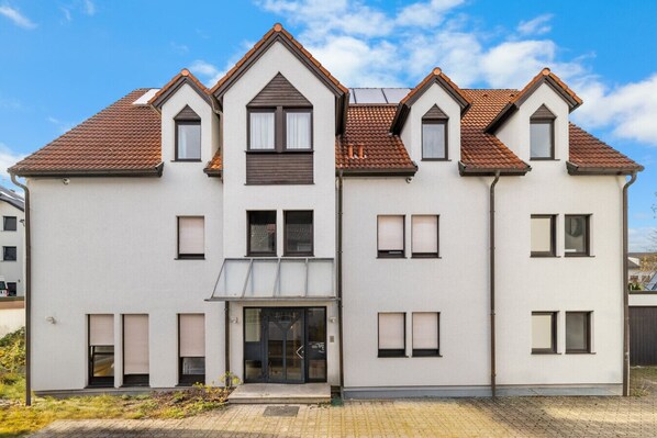 A multi-story residential building with a symmetrical facade, dormer windows, and a central entrance with a glass door.
