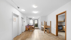 A hallway with a tiled floor, a dining area with a table and chairs, and a kitchen visible through an open door. - Havenu Oberkochen-Mitte - Doppelzimmer (Oberkochen)