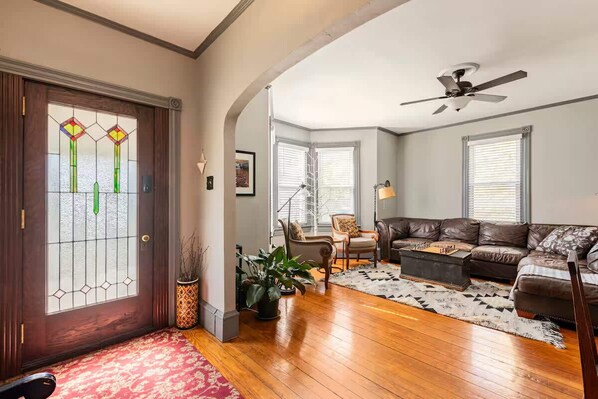 A living room with a brown leather sofa, a wooden coffee table, and a patterned rug. - Center House 1901 | Walk to Broadway | Parking (Jim Thorpe)