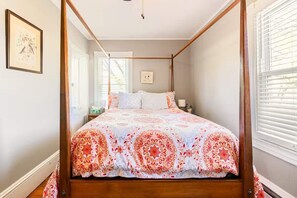 A four-poster bed with a patterned bedspread, a bedside table with a lamp, and a framed picture on the wall. - Center House 1901 | Walk to Broadway | Parking (Jim Thorpe)