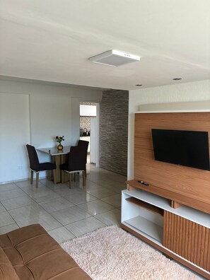 Un saló modern amb televisió de pantalla plana, zona de menjador amb cadires i una paret d'accent de pedra.