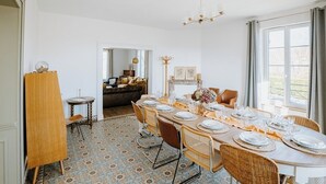 Un comedor con una mesa redonda dispuesta para seis personas, rodeada de sillas de mimbre. Se observa un caballete de madera y una pequeña mesa redonda en la esquina.