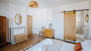 Un dormitorio con cama, cómoda de madera, una silla, un espejo y una puerta corredera que da al baño.
