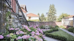 Un jardín con hortensias rosas, un muro de ladrillo y una mesa blanca con una valla metálica al fondo.