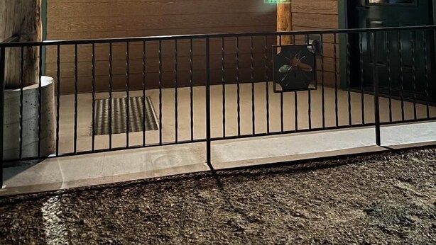 Fachada de madera con barandal metálico, una puerta y un ventanal pequeño.