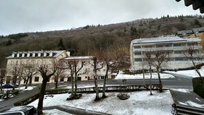 A building with a flat roof and multiple windows, surrounded by snow-covered ground and bare trees. - Family Refuge Near the Shuttle (Mont-Dore)