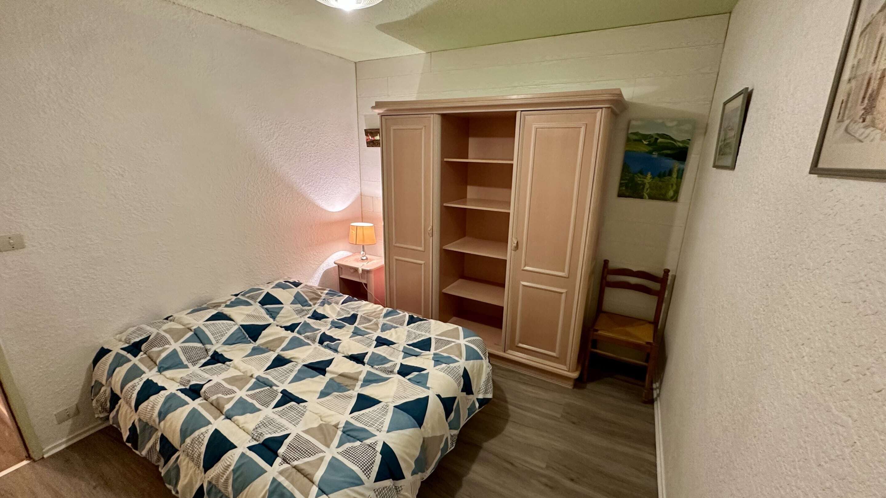 Une chambre à coucher comprenant un lit, une table de chevet, une lampe, une armoire et une chaise.