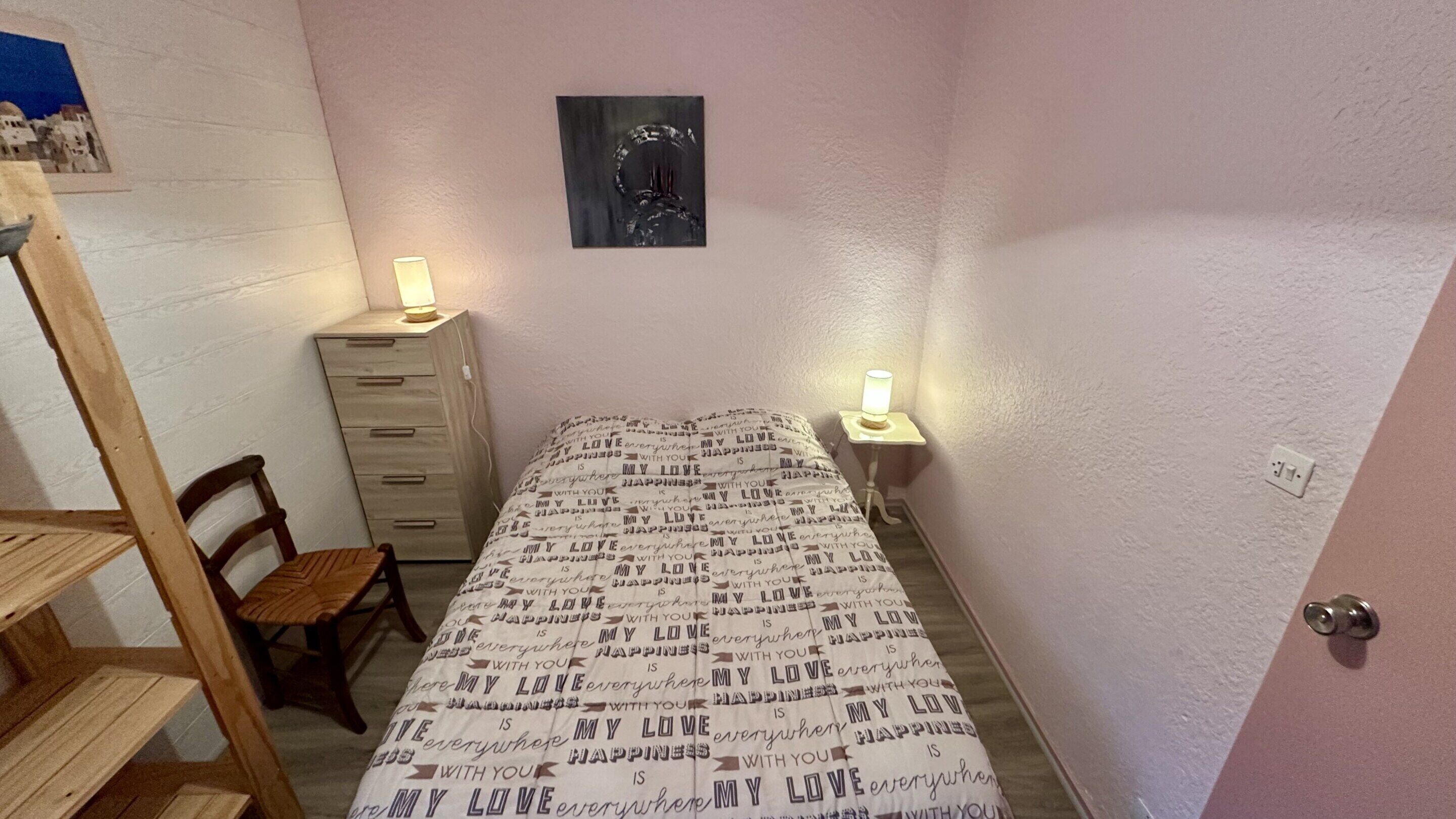A small bedroom with a bed, a wooden dresser, a chair, and two bedside lamps.