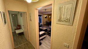 A narrow hallway with a bench, a dining area with a table and chairs, and a framed picture on the wall. - Family Refuge Near the Shuttle (Mont-Dore)