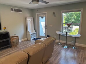 A living room with a beige sofa, a TV stand, a wicker basket, a white cabinet, and a glass table with two chairs.