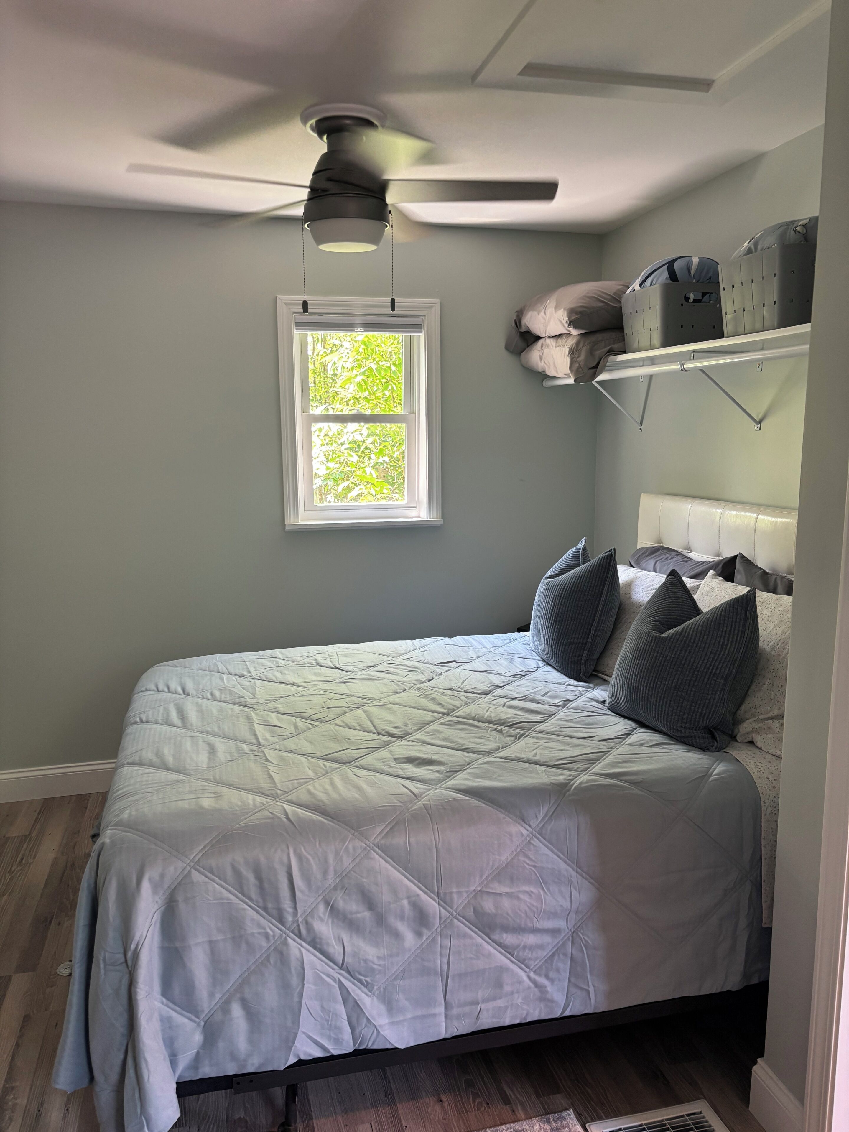 A bedroom with a bed, a ceiling fan, a window, and a built-in shelf with storage baskets.