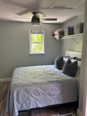 Een slaapkamer met een bed, een plafondventilator, een raam en een inbouwkast met opbergmanden.