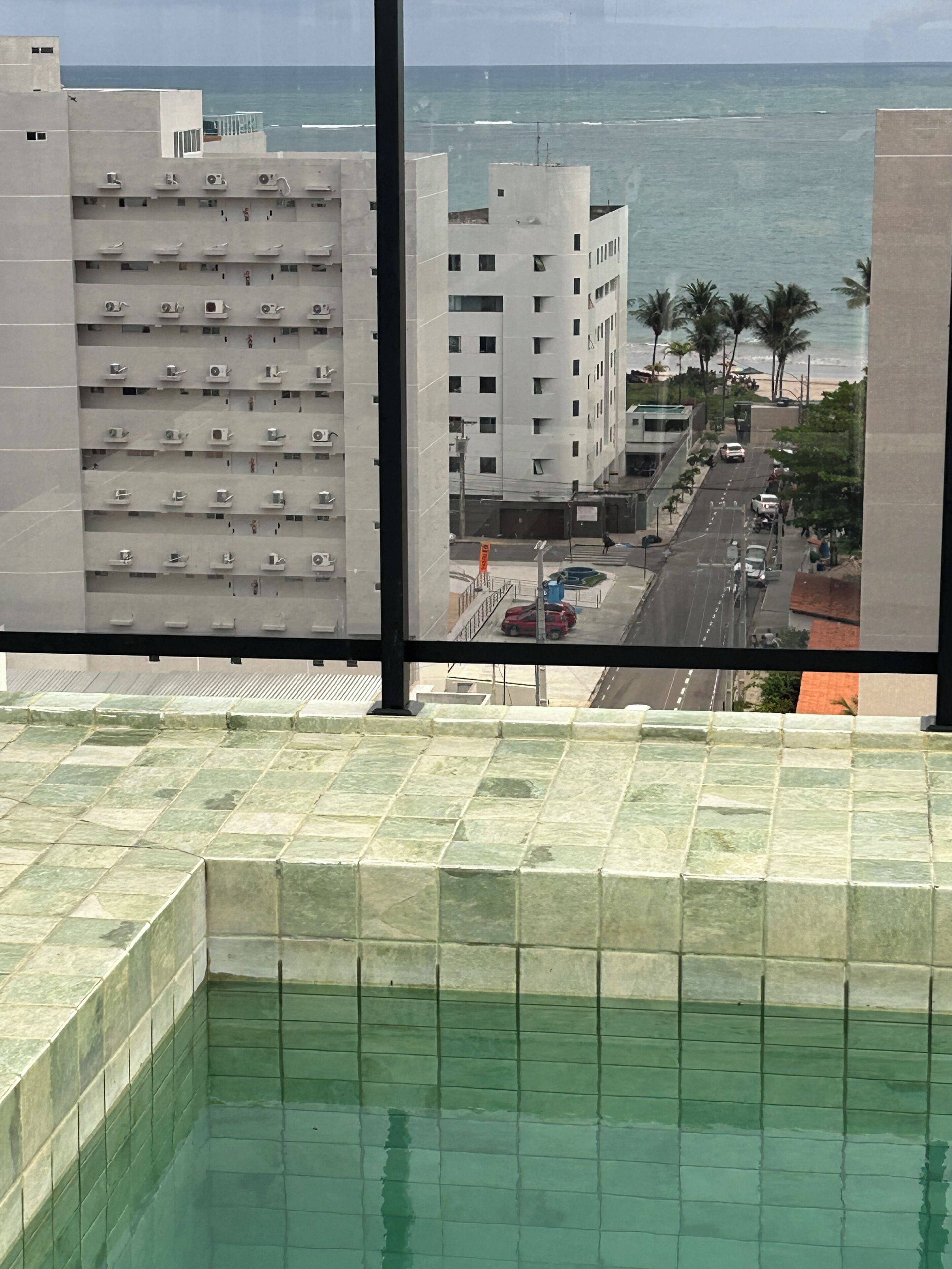 Vista desde una ventana con piscina, calle con coches y edificio con varios balcones.
