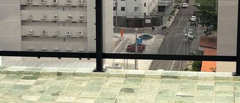 Vista desde una ventana con piscina, calle con coches y edificio con varios balcones.