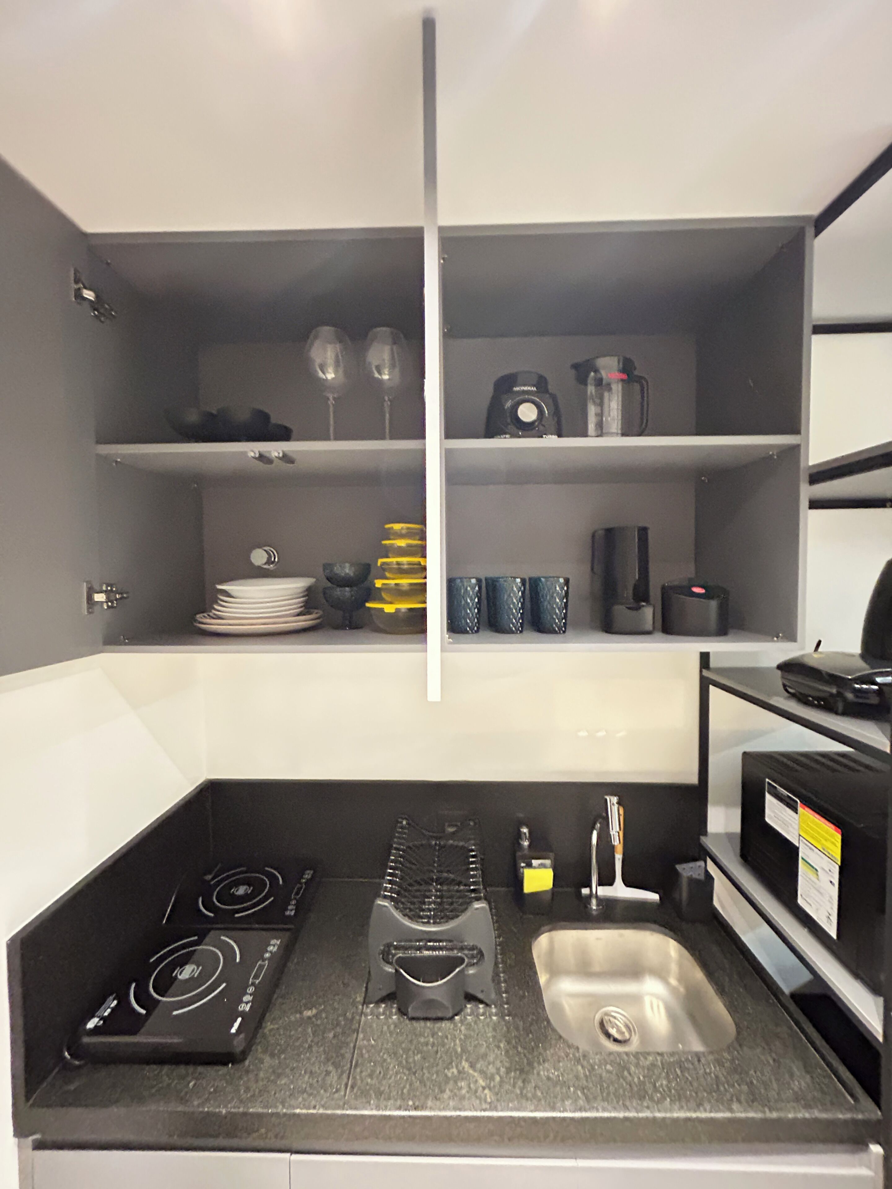 A compact kitchen with a stove, sink, and shelves containing kitchenware and appliances.