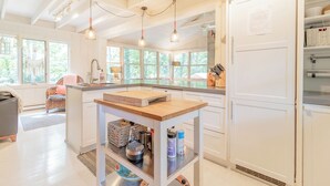 A modern kitchen with white cabinetry, a wooden island, pendant lighting, and large windows offering views of greenery. - Walk to white sand private beach of Oakwood Park - 4 bed cottage steps to lake. (Grand Bend)