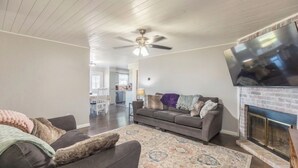 Ein Wohnzimmer mit Kamin, Deckenventilator und großem Fernseher.