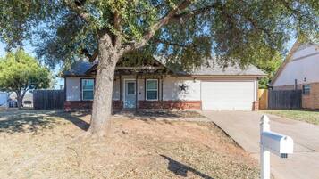 A single-story house with a garage, a mailbox, and a large tree in front.