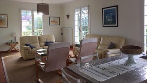 Ein Wohnzimmer mit einer Sofagarnitur, einem Esstisch mit Stühlen und einem großen Fenster, das für natürliches Licht sorgt.