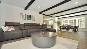 A modern living room with a grey sofa, a round coffee table, and a dining area with a table and chairs. - Stream Home (Saratoga Springs)