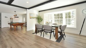A dining area with a pool table, chairs, and a window with a view. - Stream Home (Saratoga Springs)