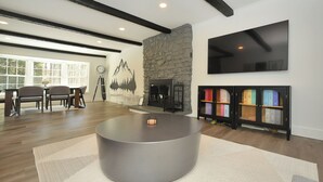 A modern living room with a stone fireplace, a flat-screen TV mounted on the wall, and a round coffee table. - Stream Home (Saratoga Springs)