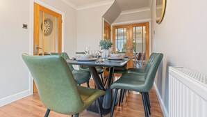 Un coin repas avec une porte à cadre en bois, une horloge et une table dressée pour quatre personnes, avec des chaises vertes.