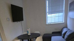 A small living area with a round table and two chairs, a grey sofa, a flat-screen TV mounted on the wall, and a window with blinds. - 1BR/1BA Comfortable & Convenient (Belleville)